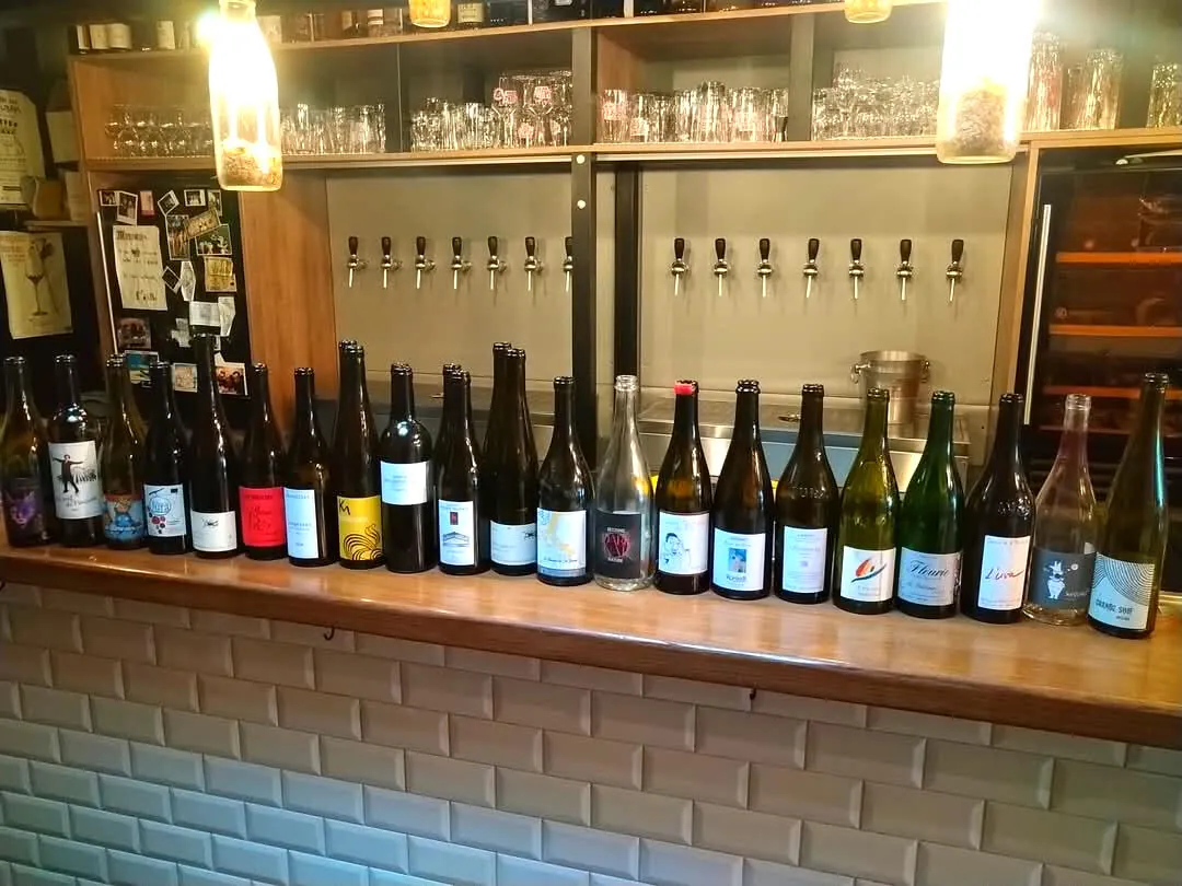 Des bouteilles de vin nature alignées sur le comptoir devant les tireuses